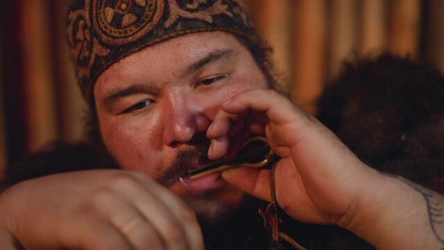 Plump man in national clothes plays vargan performing on stage at festival closeup slow motion. Mouth musical instrument. Yakut traditions