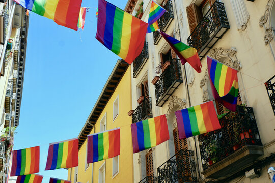 Festive flags of LGBTQ community hang between elegant retro buildings in gay friendly district Chueca in Madrid, Spain