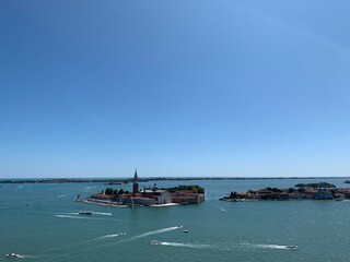 Boats at Venetian lagoon entering and leaving Venice town. Island with Church of San Giorgio Maggiore in the background. View from St. Mark's Campanile tower. Emerald blue water. Venice, Italy