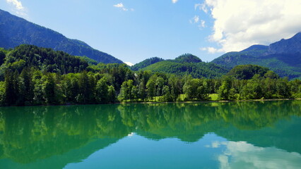schöner Blick auf Ufer des Kochelsees in Bayern mit Badestrand, Berg, Wald, blauem Himmel und Wolken