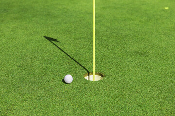 A golf ball near the hole with the flag on the golf course on the green grass