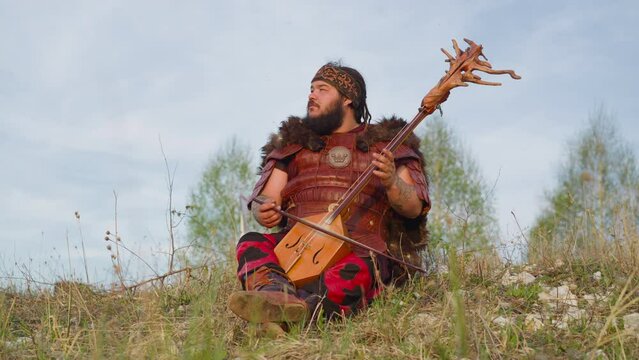 Dreaming man with overweight plays stringed instrument sitting on hill grass. Inspiring Siberian melodies. Open musical festival of Altai culture
