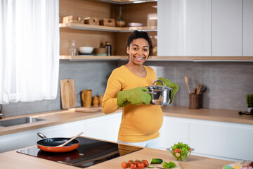 Smiling young pregnant african american woman with big belly in protective gloves prepares dinner