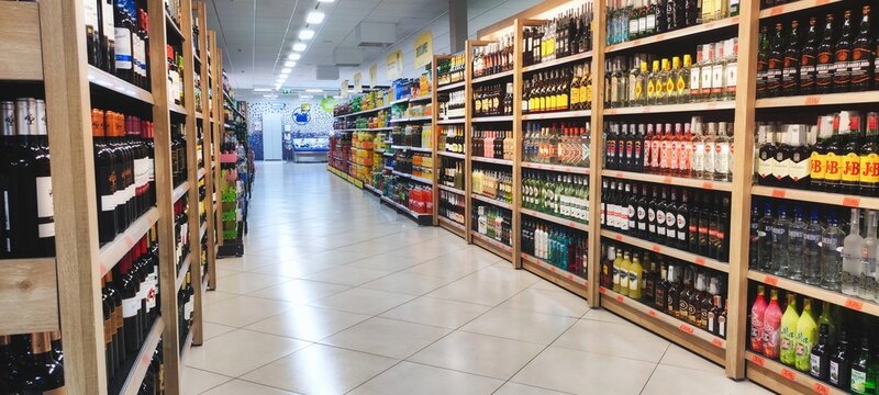 An aisle in a supermarket or off-licence with alcoholic drinks on the shelves, and no people