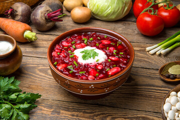 Traditional Ukrainian borscht with beetroot beans meat and vegetables in a ceramic bowl with ingredients on an old wooden rural table. Selected focus. - 516333475