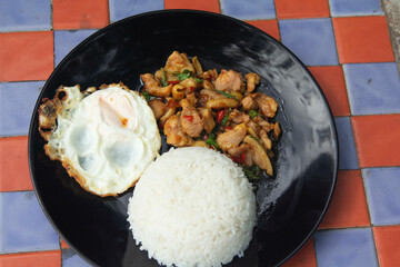 Basil, chicken, fried egg, Thai food The house style is not upscale in a black ceramic plate placed on a plaid concrete table. Ready to serve and delivery