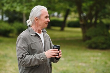 Senior man in stylish outfit holding cup of coffee.