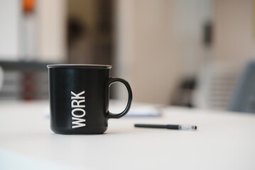Cup of coffee with inscription WORK on white wooden table in office