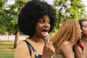 pretty afro american woman eating an ice cream in the park with friends