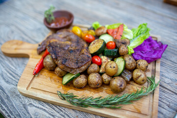 Delicious beef steak with tomato, baby potato, pepper, salad on wooden background.