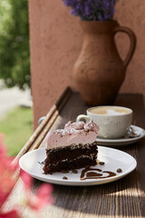 Atmosperic natural piece of cake and a glass of cappuccino on wooden table outdoor in the cafe terrace. Aesthetic coffee time. Lavander in the jug. Time for yourself. Hard shadows.