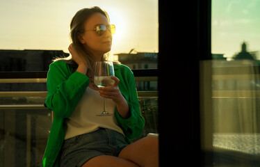 Woman with white wine enjoys the sunset on her balcony.