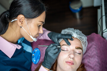 Procedure of eyebrow microblading. A master in black gloves is doing a blending needle of model's brow.