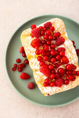 Rich sweet pie with fresh fruits, decorated with red currants and raspberries, in a plate on a pink background