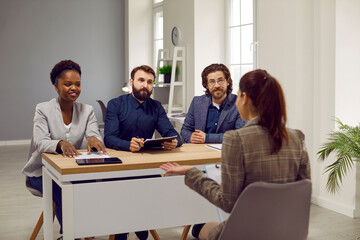 Employment and hiring. Friendly group of HR employees during interview in office talk to woman with job applicant. Three multiracial female and male colleagues are sitting at table in front of woman.