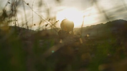Silhouette of person playing shamanic drum in grass at highland backside view. Magical ritual at sunrise light. Conservation of Siberian culture