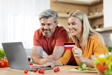 Cheerful couple making online order, using laptop at kitchen