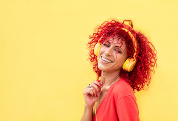 portrait of a beautiful smiling latina woman with red afro hair, wearing yellow headphones looking at the camera on a yellow background