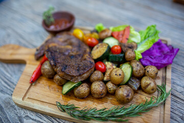 Delicious beef steak with tomato, baby potato, pepper, salad on wooden background.