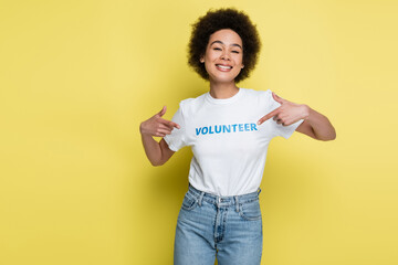 excited african american woman pointing at volunteer lettering on t-shirt isolated on yellow.