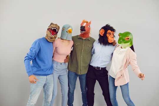Funny diverse people in animal rubber masks hug show unity and friendship at workplace. Unknown employees or workers in headwear have fun relax in office. Employment concept.