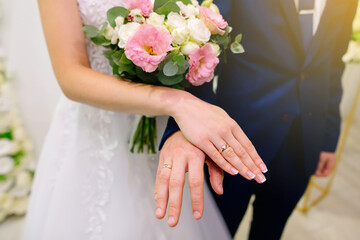 Obraz na płótnie Canvas The bride and groom show off their precious gold wedding rings. Bouquet of white and pink roses, neat French manicure of the bride. High quality photo