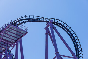 Part of a blue-purple rollercoaster against a cloudless blue sky. Extreme attraction. Metal construction.