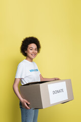happy african american woman with donate box looking at camera isolated on yellow.