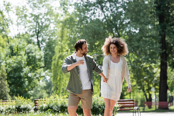 joyful young couple holding hands while walking together in summer park.