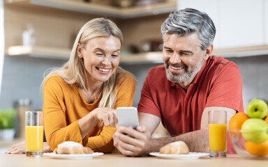 Cheerful beautiful spouses having breakfast, checking smartphone