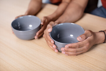 Hands of hungry young african american wife and husband holding empty plates on table in kitchen