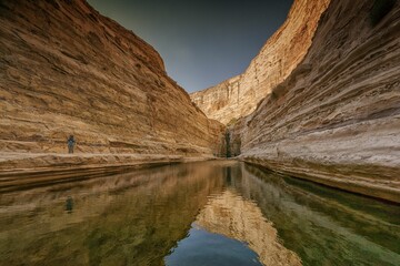 A person taking a picture of the canyon reflected in water in Ein Avdat National Park in Israel