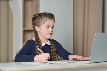 A cute school girl having online lesson using laptop and keyboard, looking at computer screen and...