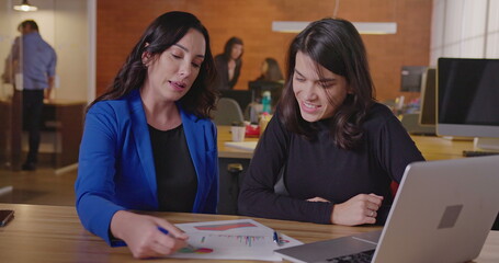 Senior business female executive looking at graphs and results with younger female staff at office workplace. Business woman coaching employee