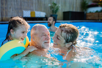 Multi generation family having fun and enjoying swimming in backyard pool.