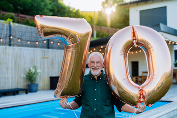Man with number 70 balloons celebrating birthday near backyard pool.