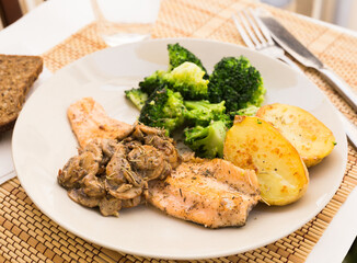 fried river trout fillet with a complex side dish of broccoli, baked potatoes and mushroom sauce