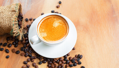 Top view of coffee cup has golden foam and mixed or blend coffee beans in a brown sack on wooden backgrou