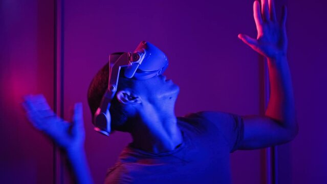 Man in a virtual reality helmet illuminated in red and blue plays a game. Young man in VR headset moves his hands in virtual space. Futuristic technology to play simulation 3D video games Metaverse 4K