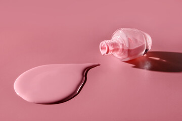 Nail polish flowing from an overturned bottle on a pink background.