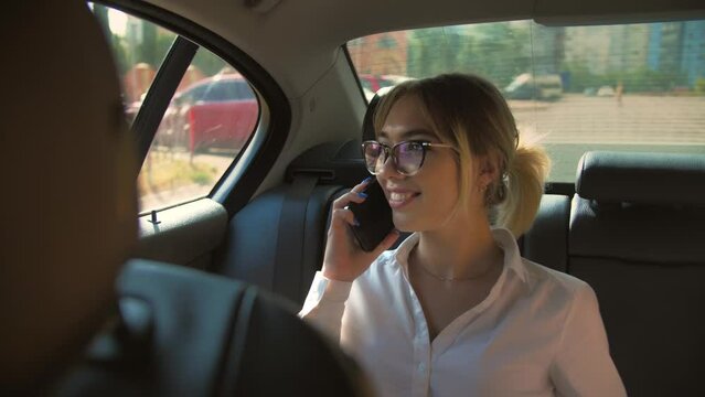 Attractive Young Woman in Car Using Mobile Phone. Female Blonde on Backseat of Ride Sharing Transportation Talking on Smartphone.