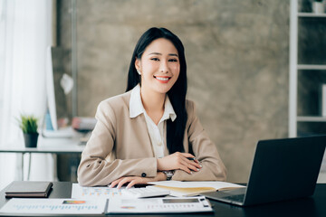 Portrait of attractive woman sitting at office desk, writing on notebook and looking at laptop screen