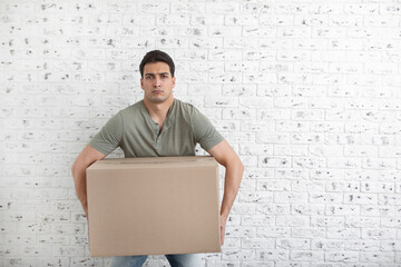 Funny man holding heavy box on white brick background