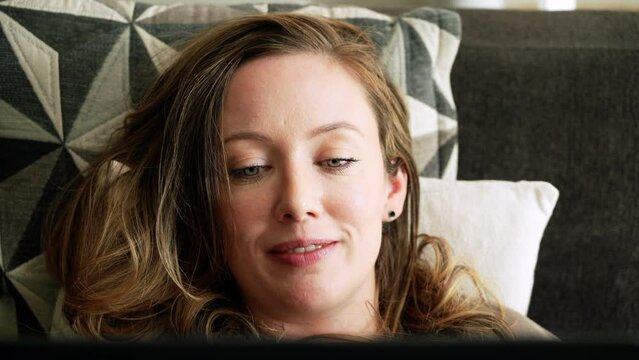 Caucasian woman relaxing at home, lying on a sofa, catching up with friends and family on her laptop computer.