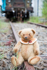 cute brown teddy bear sits alone on empty mini-rails and looks into the distance