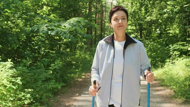 50s years old woman training Nordic walking in park outdoors. Weekend leisure activity