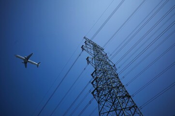 Low angle shot of an airplane flying above the electric power transmission lines against a blue sky