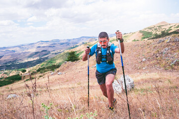 active man training uphill with poles on mountain with trail running