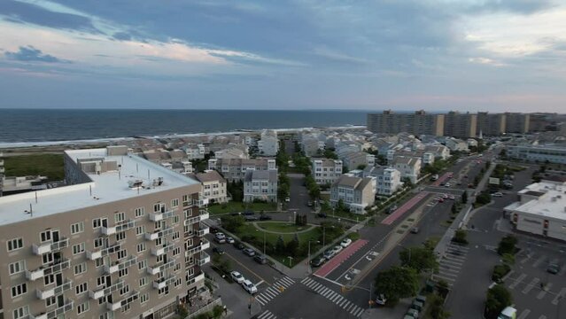 An aerial view over a strip mall roof in Arverne, NY. The drone camera dolly in and pan left down a street heading towards the beach on a beautiful evening during a cloudy sunset.