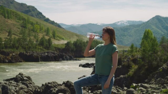 Thirsty woman drinks mineral water on bank of mountain river